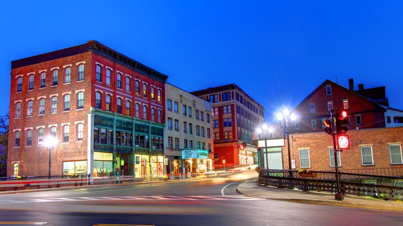 Main Street in downtown Brattleboro at dusk, brick storefronts and the lit Latchis Theatre marquee along the block
